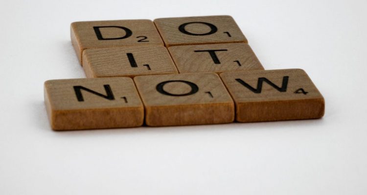 Wooden Scrabble tiles spelling 'Do It Now' on a white background. Motivational concept.