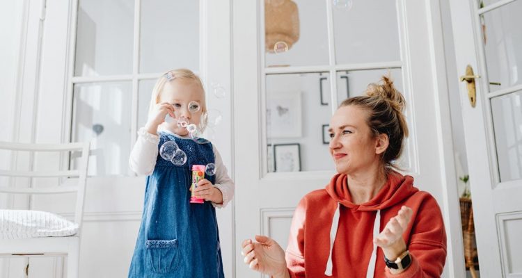 A joyful moment of a mother and daughter playing with bubbles indoors.
